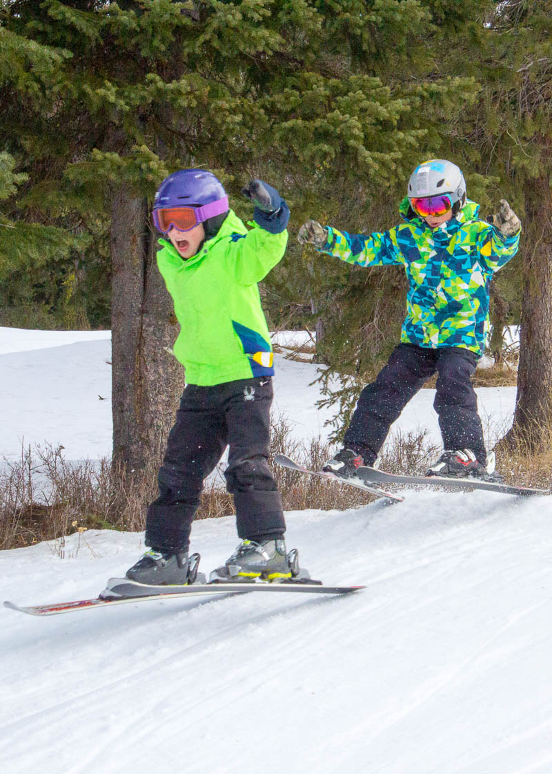 two kids hitting a jump on skis