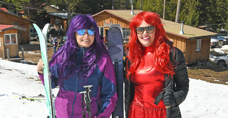 One women in purple wig and ski clothes another women in red wig and red shimmery ski outfit